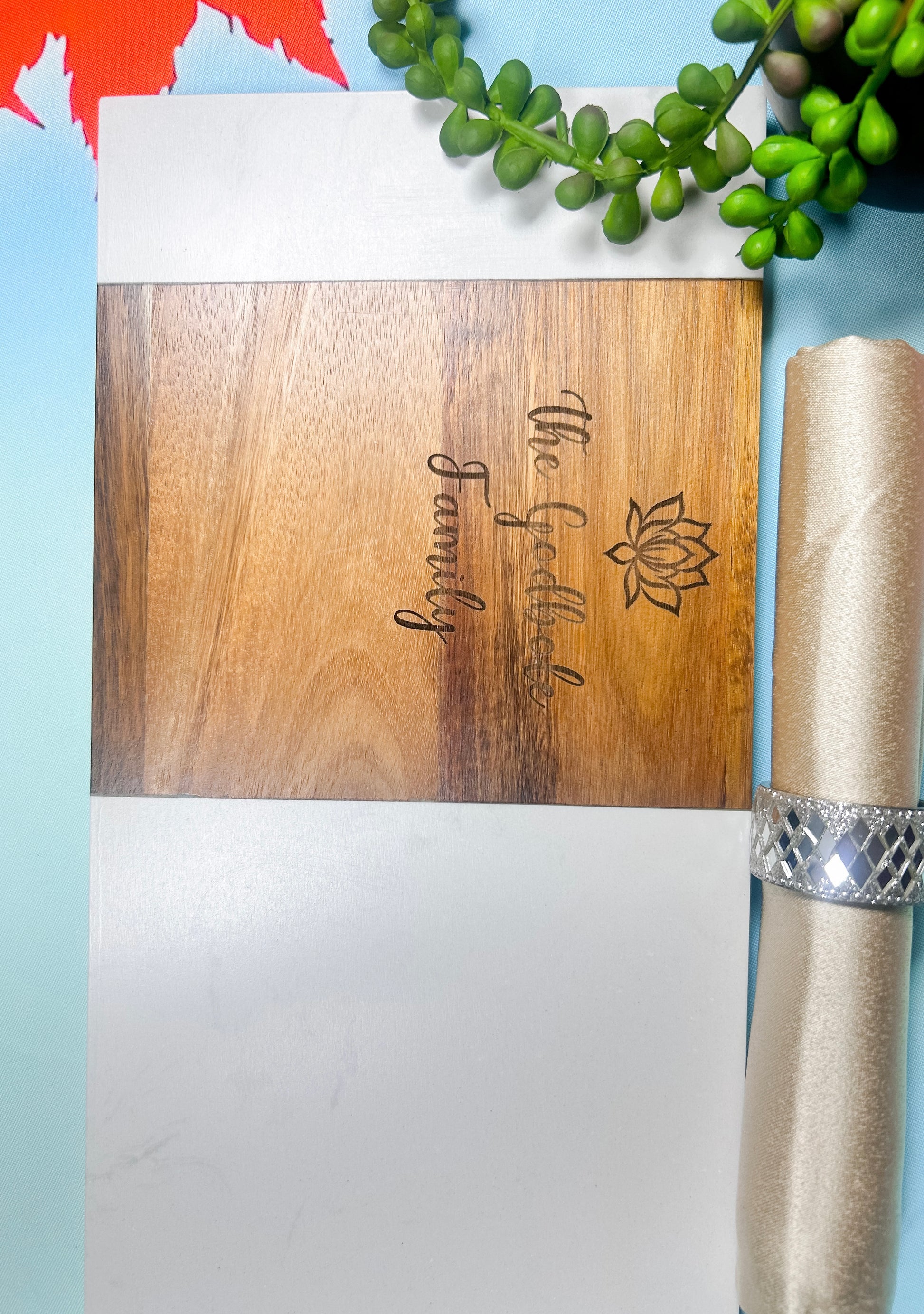 Custom engraved wood and white resin cutting board with family name and lotus design, styled with table decor