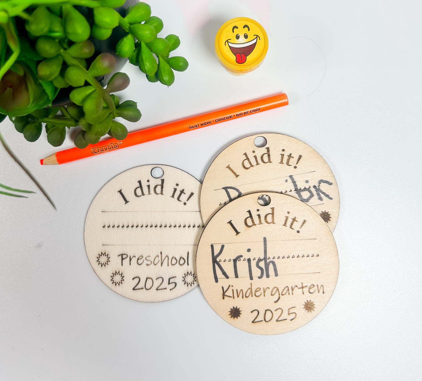 Three wooden tags with 'I did it!' and personalized text on a light background with a pencil and plant.
