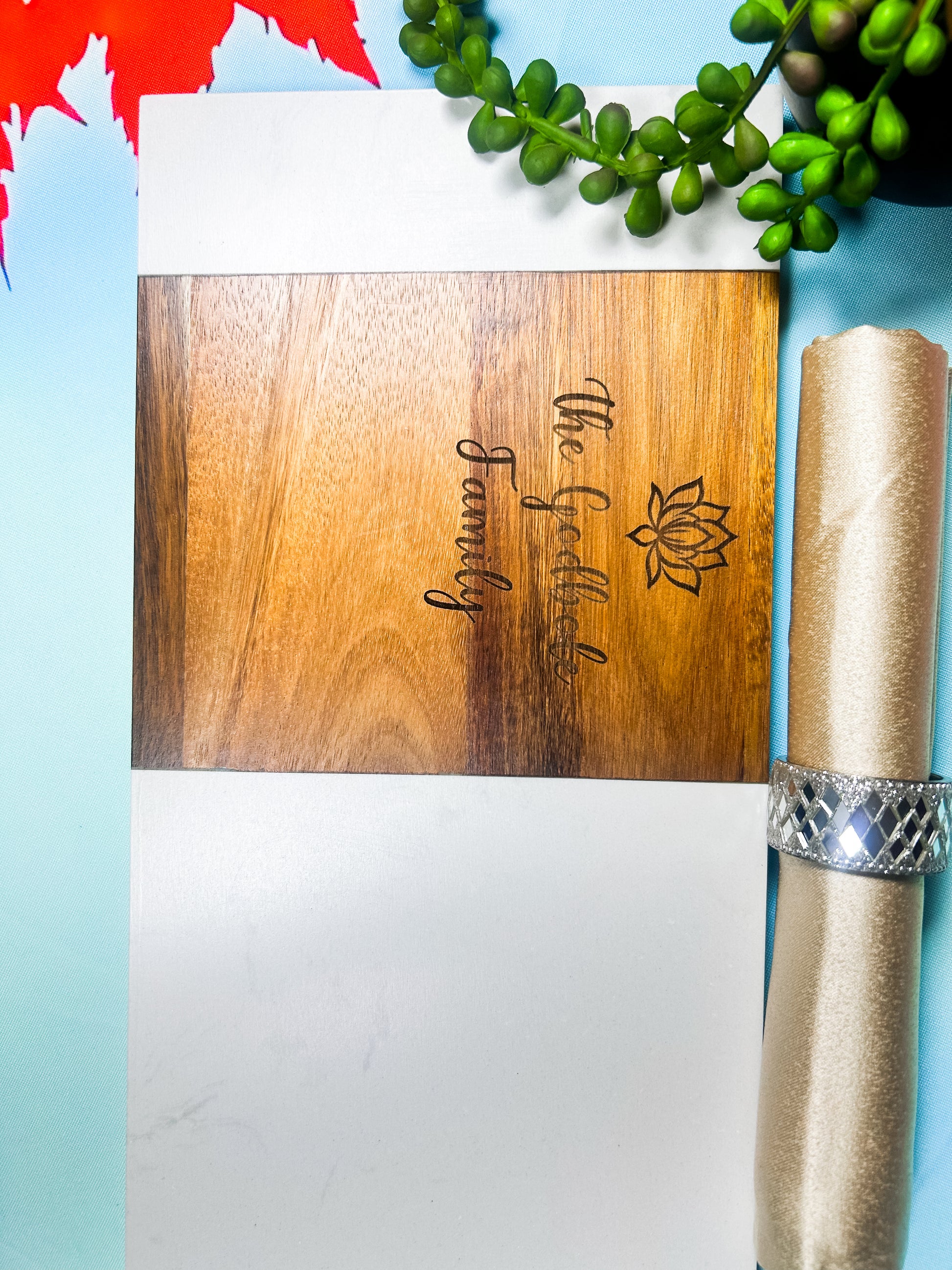 Wooden cutting board with engraved text and logo, rolled paper, and decorative elements on a light blue background.