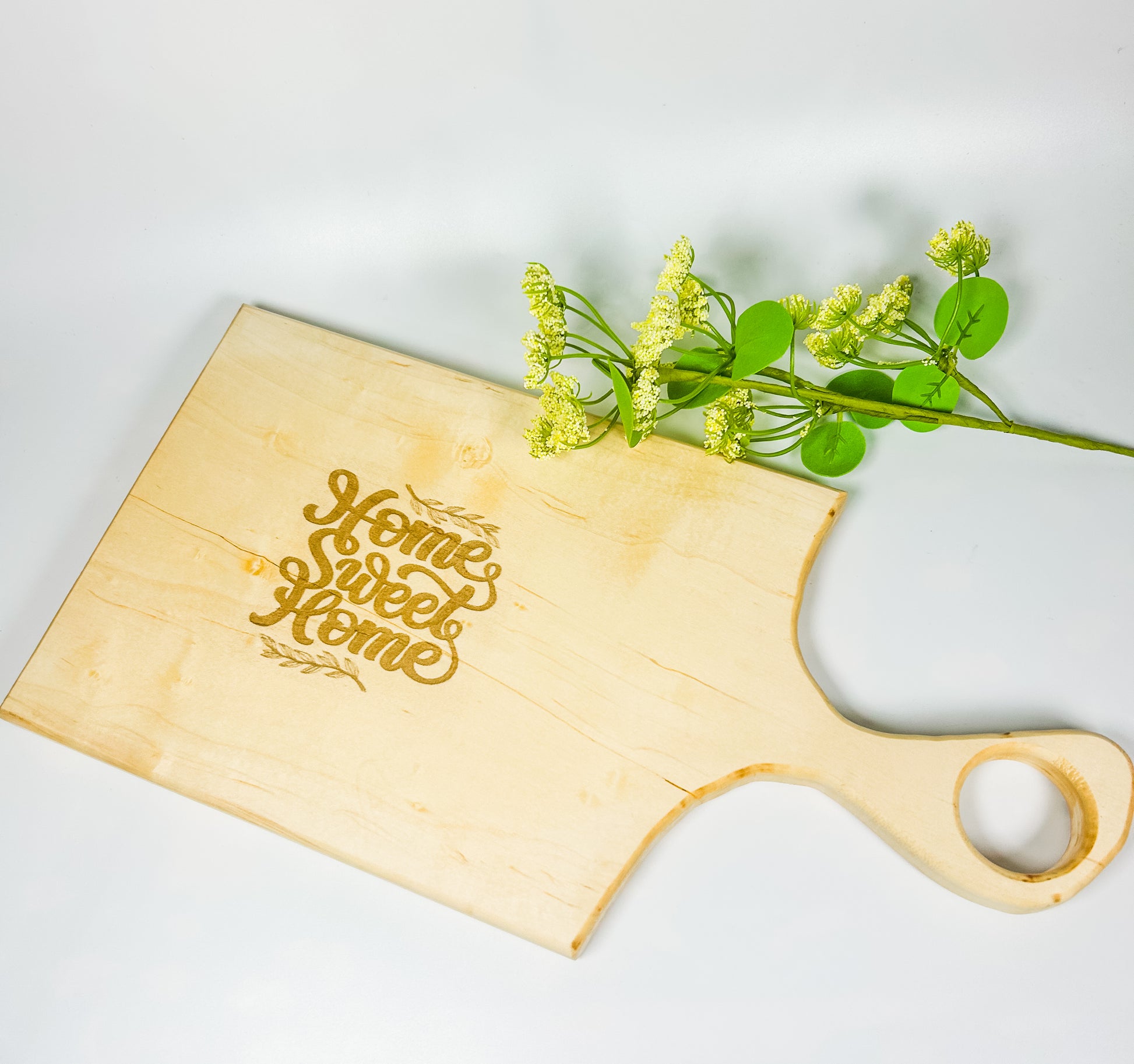 Wooden cutting board with 'Home Sweet Home' engraving and a sprig of greenery on a light background