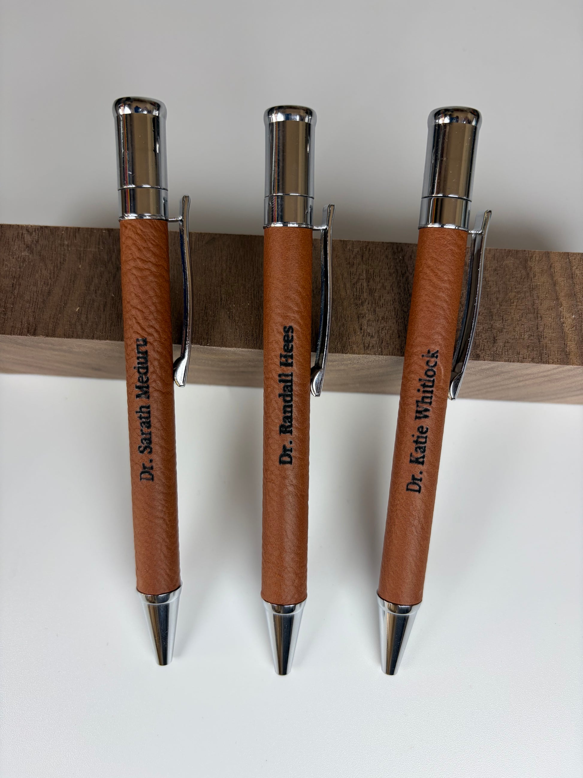     Premium brown leather laser engraved pens featuring personalized names and chrome accents for business and everyday writing.